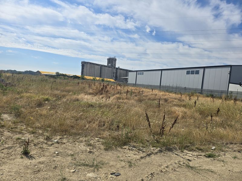 Grassy land with an industrial hall and silo in the background