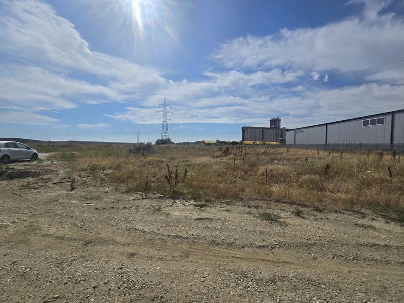 Wide site view with an unpaved edge, power pylon and industrial hall