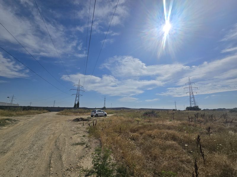 Unpaved area of the property with several high-voltage pylons and halls in the background