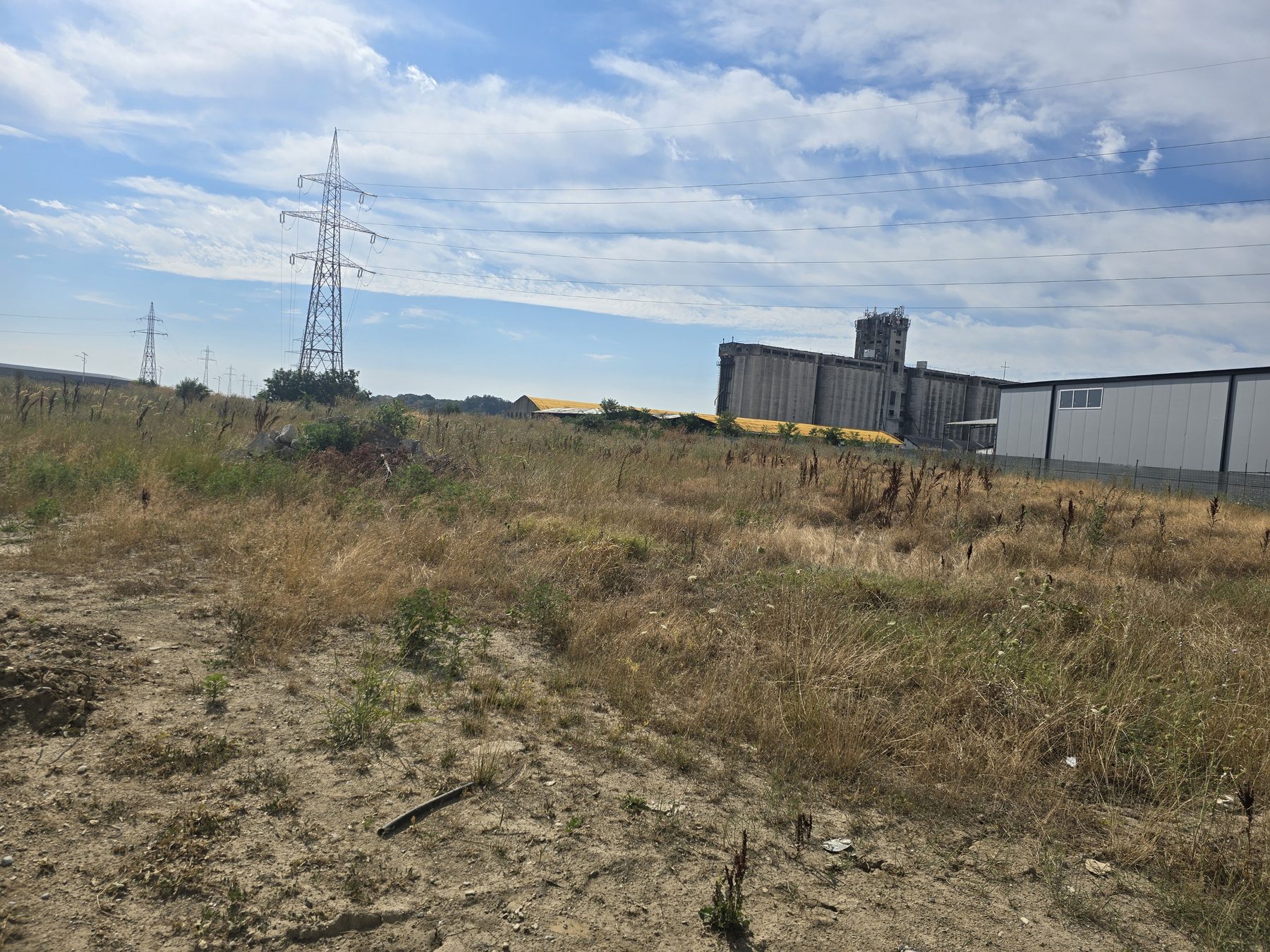Undeveloped grassy land with power pylons and industrial buildings in the background